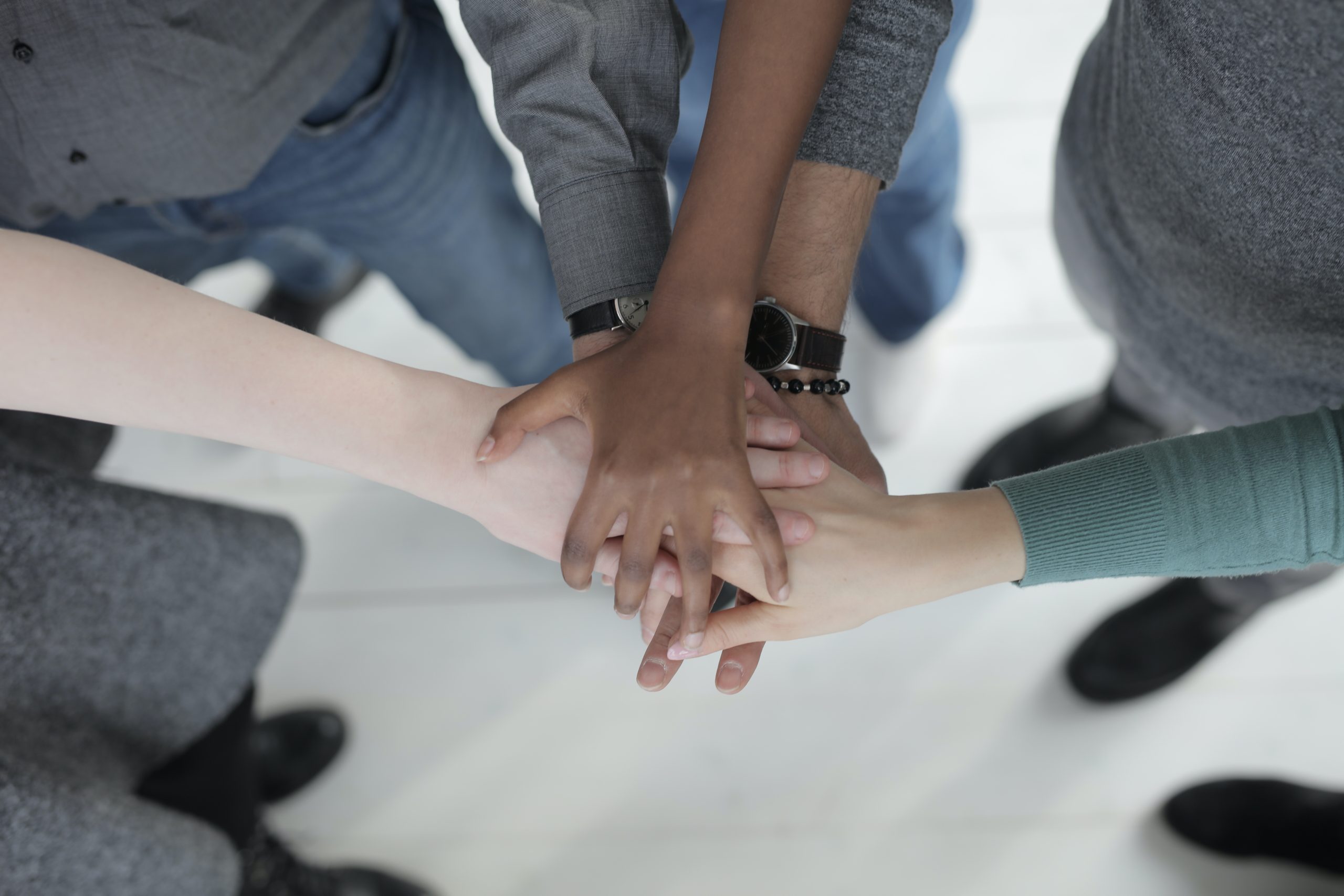 A group of people putting their hands in a huddle, symbolizing teamwork.