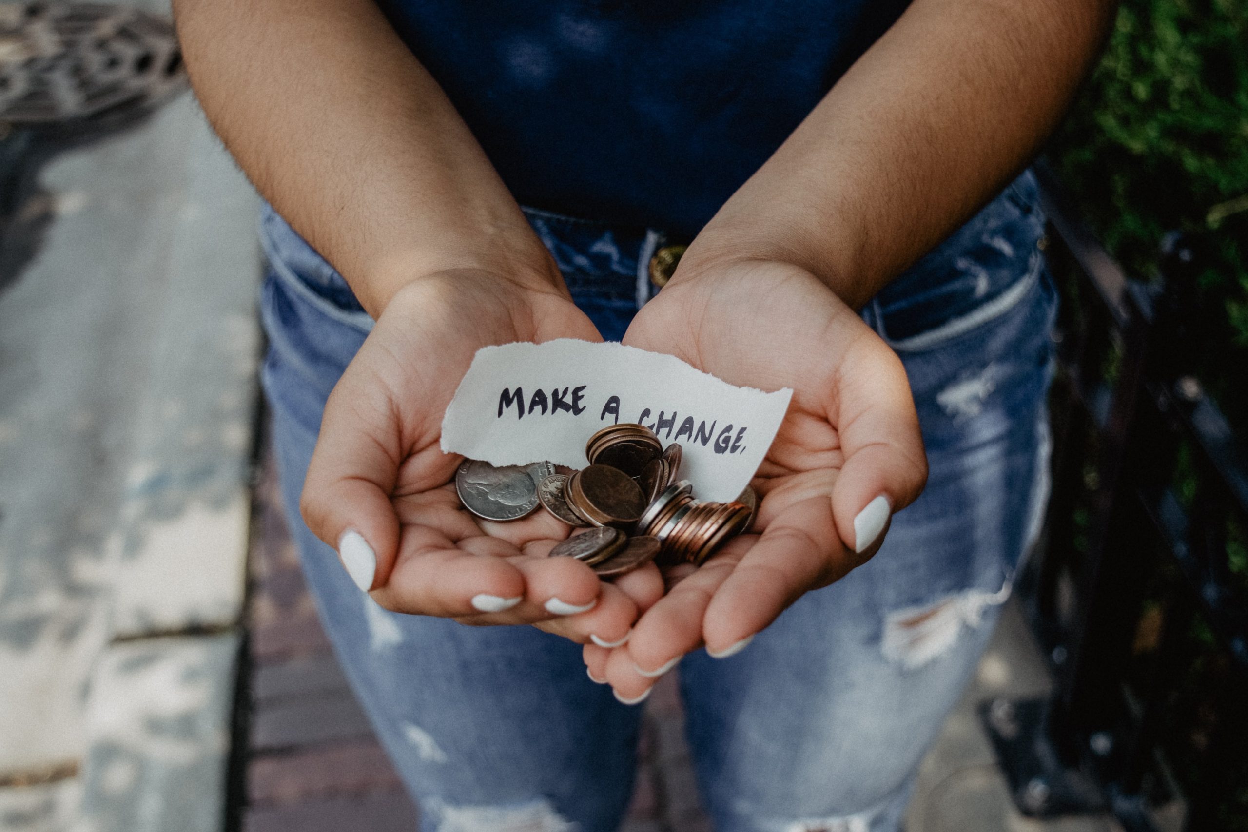 A person holding change their hand with a small sign that says make a change