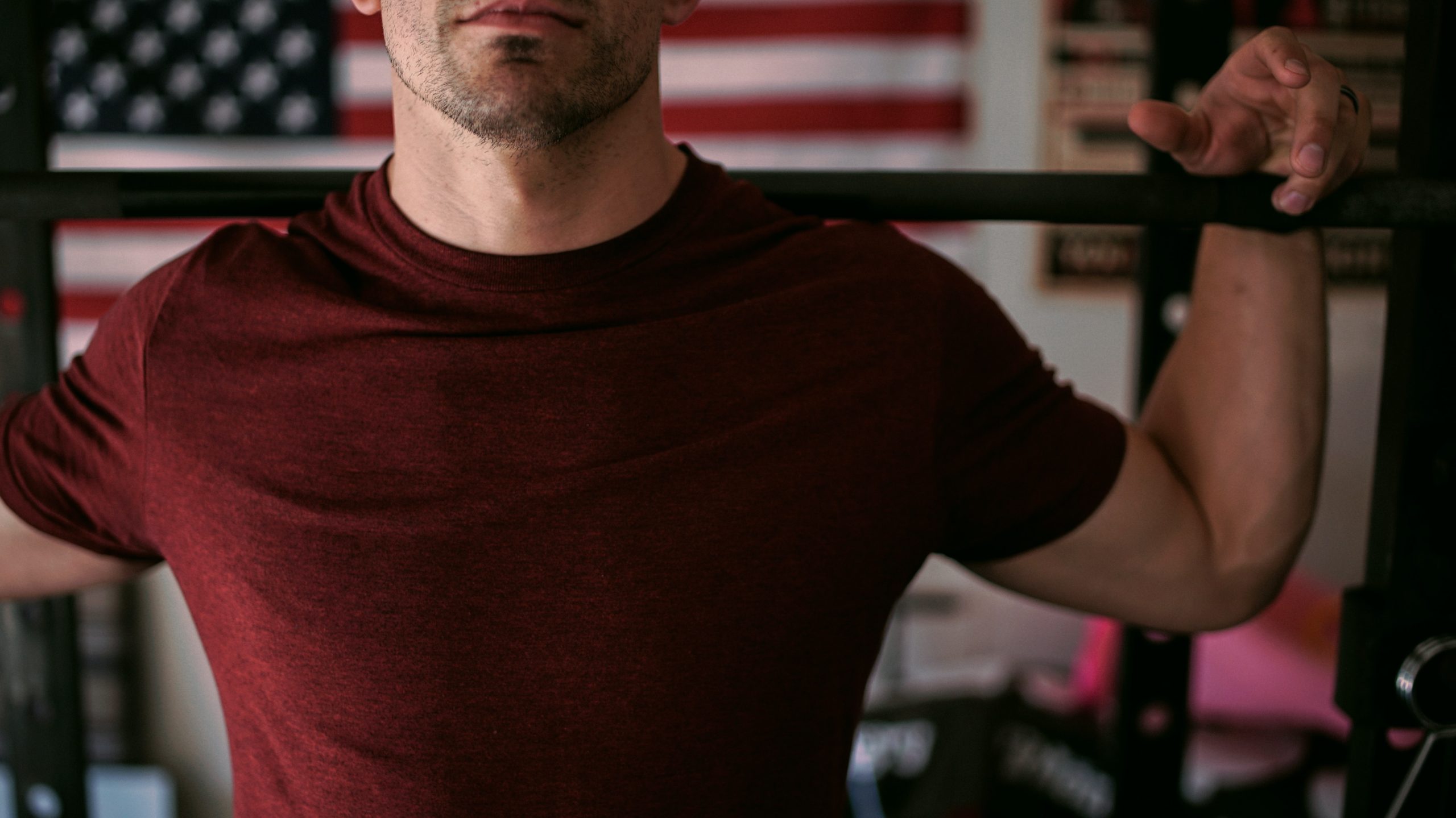 A man holding on to a barbell with an American flag in the background.